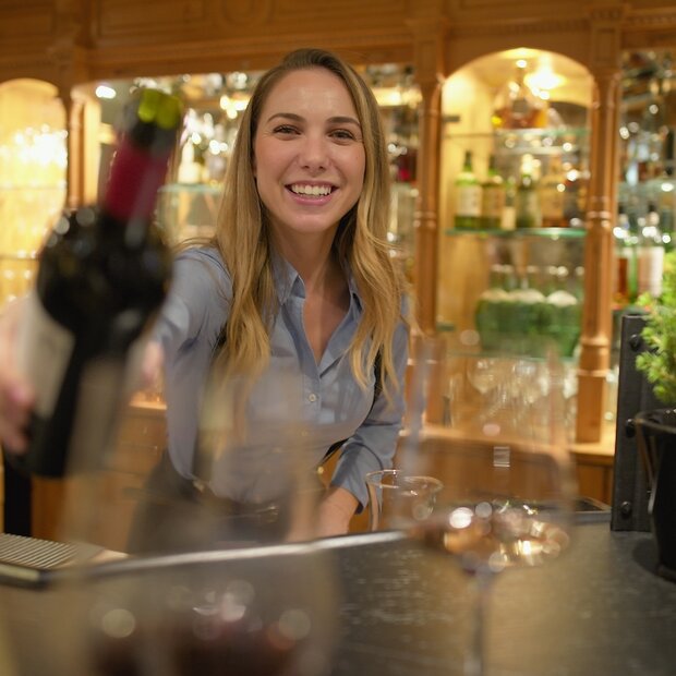 Freundliche Barkeeperin reicht Rotweinflasche über Theke