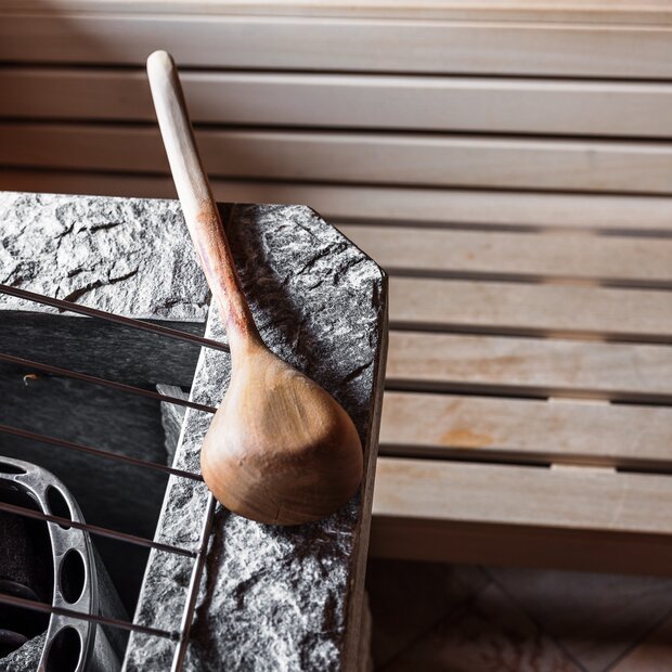 Wooden sauna ladle on stone oven in sauna