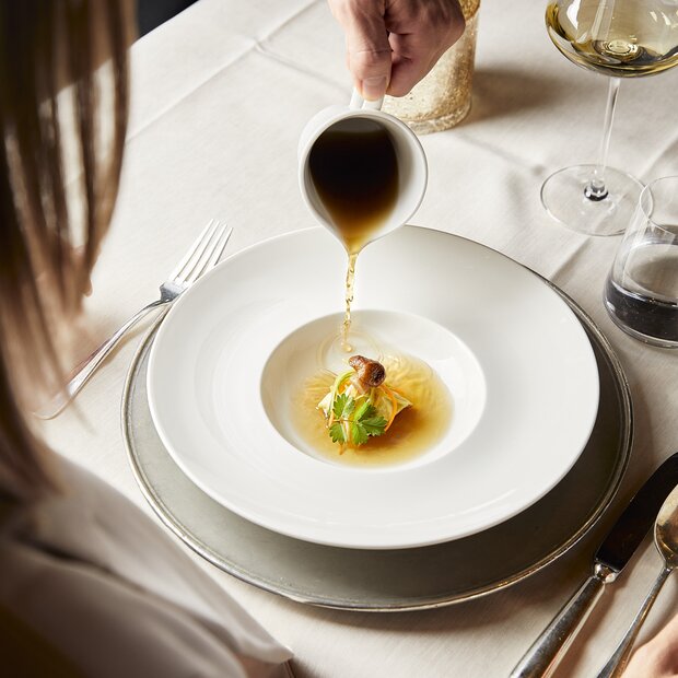 Waiter pours broth into soup bowl at the table