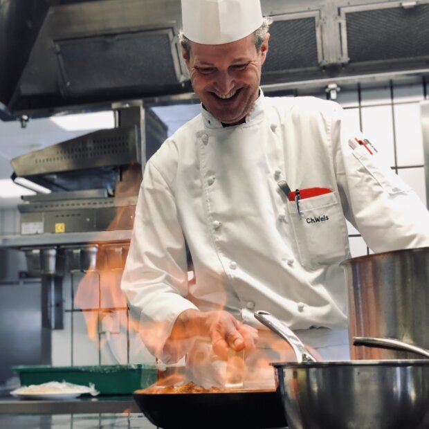 Smiling chef flambés dish in restaurant kitchen