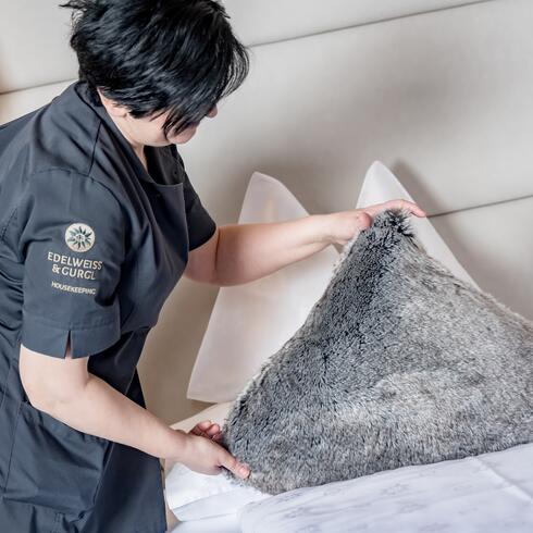 Employee arranges fluffy pillow on hotel bed