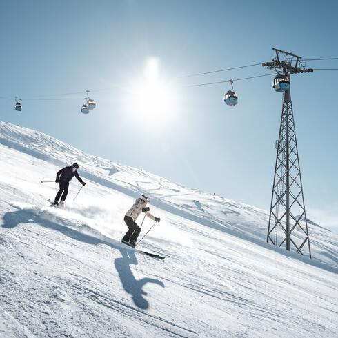 Two skiers on a sunny ski slope with a cable car