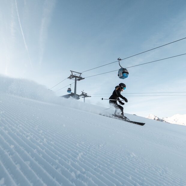 Skifahrer auf präparierter Piste unter Gondelbahn