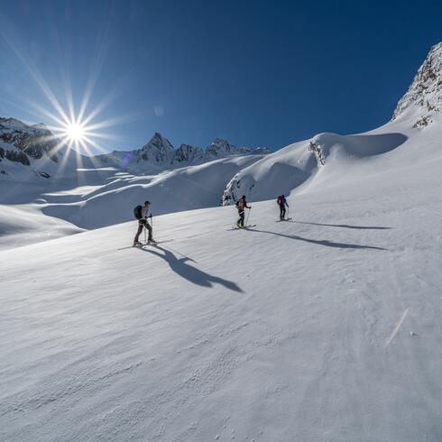 Three ski tourers in a sunny winter mountain landscape